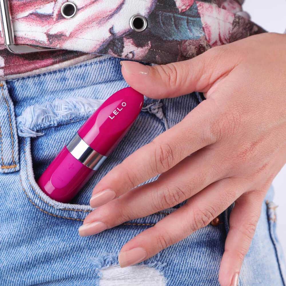 Person placing the red LELO Mia 2 vibrator, a small lipstick-shaped vibrator with 6 speeds, into the front pocket of blue ripped jeans.